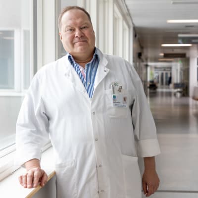 Infektioylilääkäri Markku Broas seisoo sairaalan käytävällä. Yllä on valkoinen lääkärintakki.