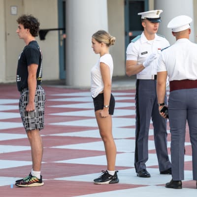 Kaksi alokasta seisoo asennossa. Kaksi laivastouniformuun pukeutunutta sotilasta puhuttelee kolmatta alokasta.