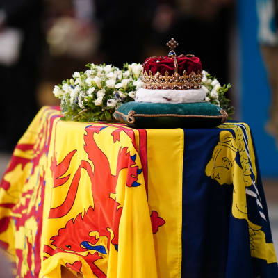 Drottning Elizabeths kista draperad med den brittiska kungliga flaggan i skotsk version. På kistan finns en blomsterhyllning och den skotska kronan vilande på en kudde.