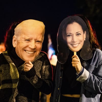 Kaksi Bidenin ja Harrisin vaalivoiton juhlijaa pitävät kasvoillaan Bidenin ja Harrisin naamareita Washingtonissa.