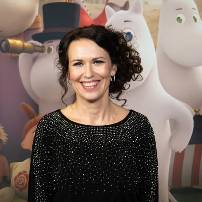 Gutsy Animations -tuotantoyhtiön luova johtaja Marika Makaroff poseeraa hymyillen kohti kameraa muumiaiheisen kuvan edessä. 