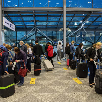 Resenärer med kappsäckar står vid Finnairs check-in-kiosker på Helsingfors-Vanda flygplats.