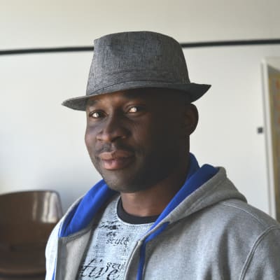 porträtt av francis oyeyiola. han bär en grå hatt, en grå tröja och tittar in i kameran.