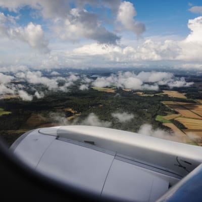 En bild tagen genom ett flygplansfönster. Utanför fönstret syns en vy över åkrar i Finland. Bilden är tagen i september 2020.