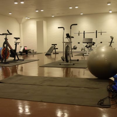 Ett gym med gymnastikmattor på golvet, motionsscyklar och andra motionsredskap.