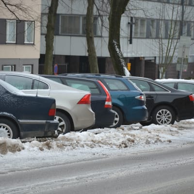 Flera bilar står parkerade i rad vintertid. 