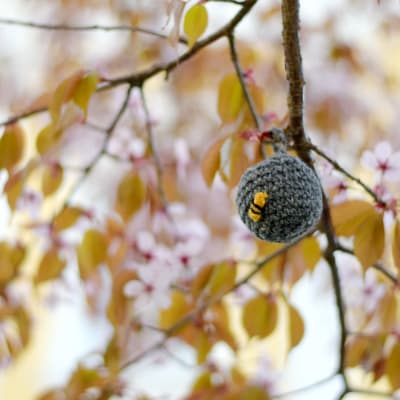 En virkad boll som ser ut som ett getingbo är upphängt i ett träd som blommar.