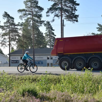 En cyklist cyklar på en riksväg. Framför cyklisten kör en lastbil.