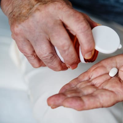 Åldrade händer häller ut en tablett från en medicinburk i handflatan.