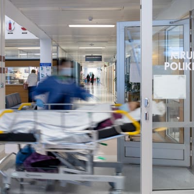 Patient i sjukhussäng rullas in genom en dörr på sjukhus. 
