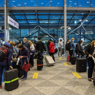 Resenärer med kappsäckar står vid Finnairs check-in-kiosker på Helsingfors-Vanda flygplats.