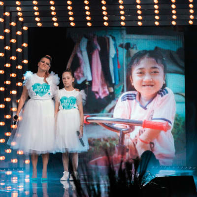 Laulaja Saara Aalto ja lapsikuoron jäsen seisovat Nenäpäivän esiintymislavalla vierekkäin valkoiset mekot yllään.
