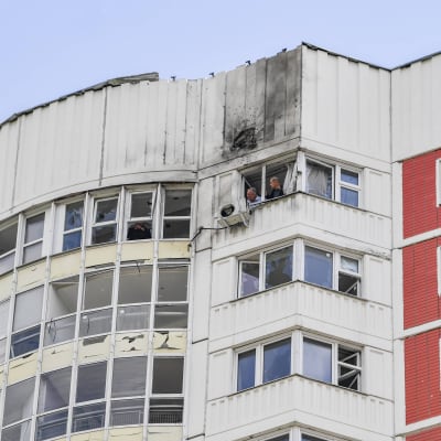 Två män tittar ut från fönstret på högsta våningen i ett höghus i Moskva. Något har träffat byggnadens fasad och exploderat.