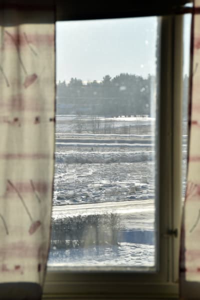 Vy över snöiga åkrar sedd genom ett fönster.