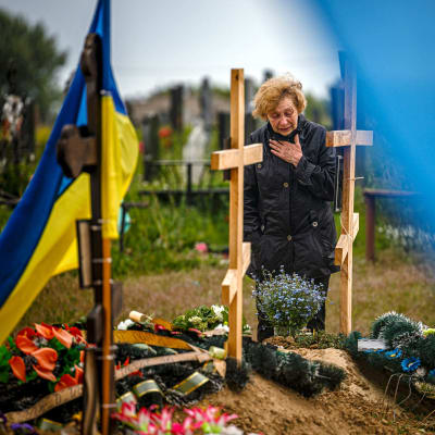 En sörjande kvinna vid en grav, men Ukrainska flaggor på gravgården och blommor på gravarna.