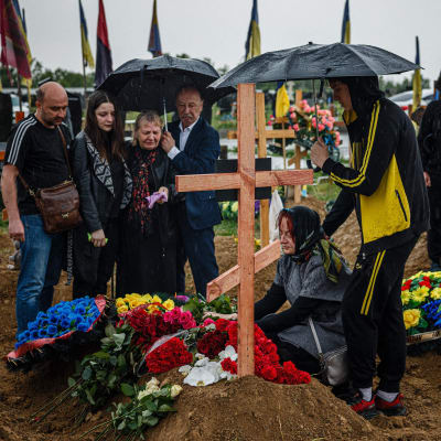 En samling människor med paraplyer på en begravningsplats omgivna av träkors.