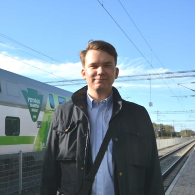 Jacob Storbjörk står på perrongen vid Bennäs tågstation i Pedersöre framför ett VR-tåg av modellen Intercity