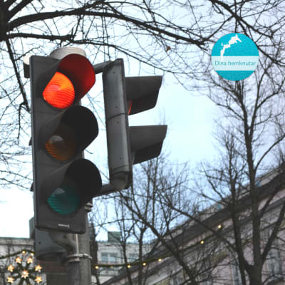Närbild på ett trafikljus som lyser rött. I övre högra hörnet av bilden finns det en rund, blå etikett där det står Dina hemknutar.