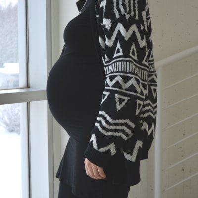Gravid kvinna står vänd i profil mot kameran vid ett fönster
