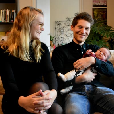 Petronella Nordman och Markus Bergfors sitter i en soffa och skrattar. I famnen håller Markus två månader gamla sonen Roy.