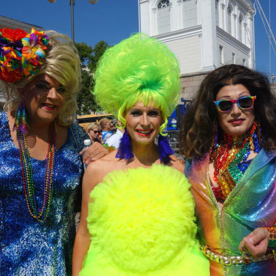 Tre pridedeltagare klädda i färggranna och glittrande kläder och peruker under Helsingfors prideparad 2016.