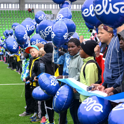Juniorfotbollsspelare med ballonger på rad på fotbollsplan när Sandvikens stadion invigs.