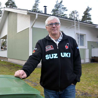En man som står vid ett avfallskärl, i bakgrunden ett småhus.