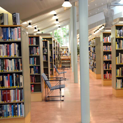En rad med bokhyllor i ett bibliotek. Orange plastmatta på golvet.