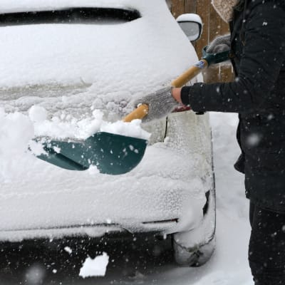 person med snöskyffel invid bil