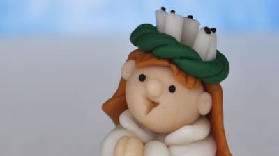 En plastfigur som föreställer en lucia med krona står på en vit bakgrund. 