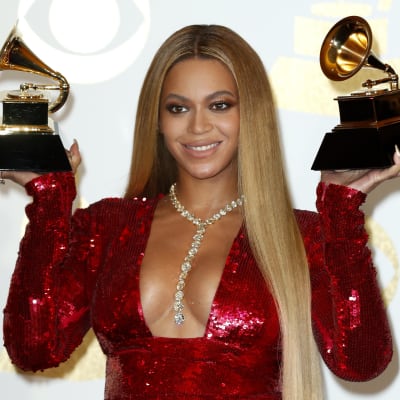 Artisten Beyoncé iklädd röd klänning håller upp två Grammy-pris.