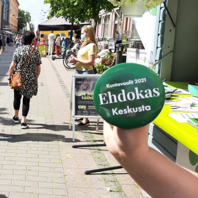 En hand håller på gågatan i Åbo upp en grön reklampins för Centern i samband med kommunalvalet 2021.