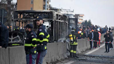 brandmän står framför en uppbränd buss. Två i bildens förgrund och en i bakgrunden.