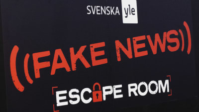 Texten Fake News Escape Room skrivet med röd och vit text på svart bakgrund.