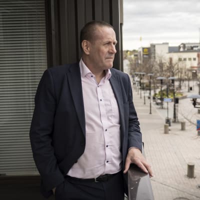 Mies seisoo kerrostalon parvekkeella ja katselee katunäkymää.