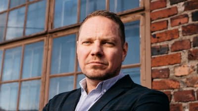 Andrteas Ödman ute vid ett fönster med små rutor och en tegelvägg 