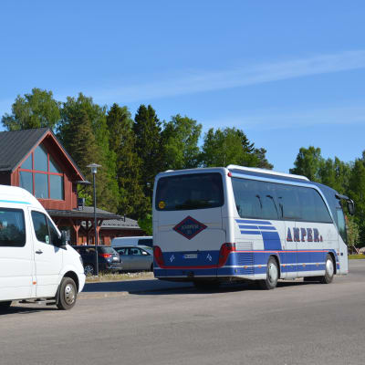 En större taxi och en buss står parkerade vid en affärsfastighet i rött trä.