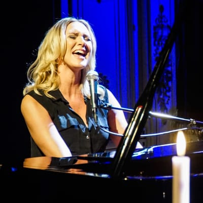 Sanna Nielsen vid en svart flygel med levande ljus i förgrunden.