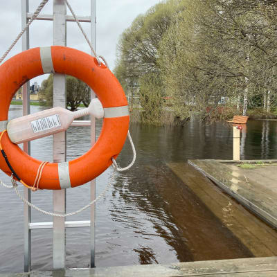Pelastusrengas telineessä Tornion Nordbergin rannassa. Tulvavesi on noussut laajalle, taustalla näkyy veden ympäröimä penkki.