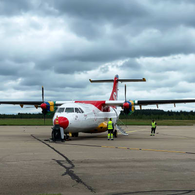 Danish air transport -yhtiön (DAT) punavalkoinen ATR-potkuriturbiinikone Kajaanin lentokenttätasolla, taustalla taivaalla synkkiä sadepilviä.