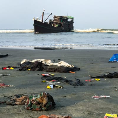 En del av de räddade rohingyernas ägodelar låg kvar på stranden nära Teknaf på torsdag morgon. Det är oklart om trålaren i bakdrunden är den båt som de drivit omkring på i nästan två månader. 