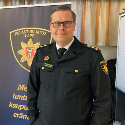 Lapin pelastuslaitoksen pelastusjohtaja Markus Aarto palomiehen univormussaan, taustalla Lapin pelastuslaitoksen mainosroll-up.