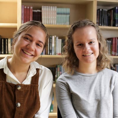 Elin Fierens och Anna-Sofia Paavonen sitter framför bokhyllor fulla med böcker.