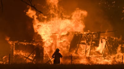 En brandman står i förgrunden, i bakgrunden brinner ett hus.