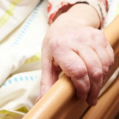 En gammal persons hand håller i ett sängräcke.