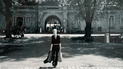 Säveltäjä, muusikko Astrid Swan kävelee Suomenlinnassa kohti porttia. Kuvassa selin, pitkät hiukset poninhännällä ja käsissään kassi sekä farkkutakki.