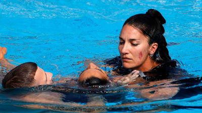 Anita Alvarez hjälps från bassängen av tränaren Andrea Fuentes och en badvakt.