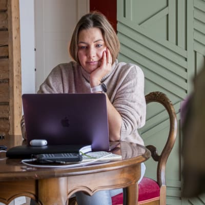 En kvinna sitter och jobbar på sin laptop i ett vardagsrum.