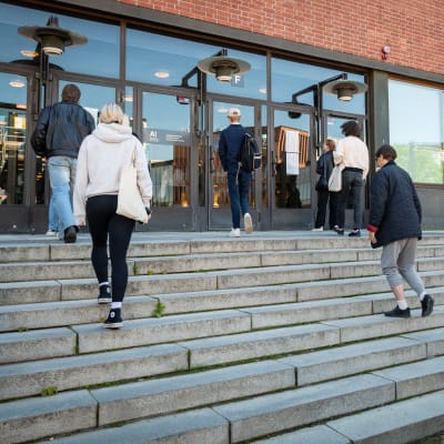 Ihmisiä saapumassa korkeakoulun pääsykokeisiin Aalto-yliopiston kauppakorkeakoulussa.