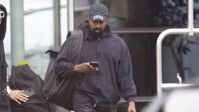Kanye West iklädd keps med trycket 2023 och en telefon i handen.